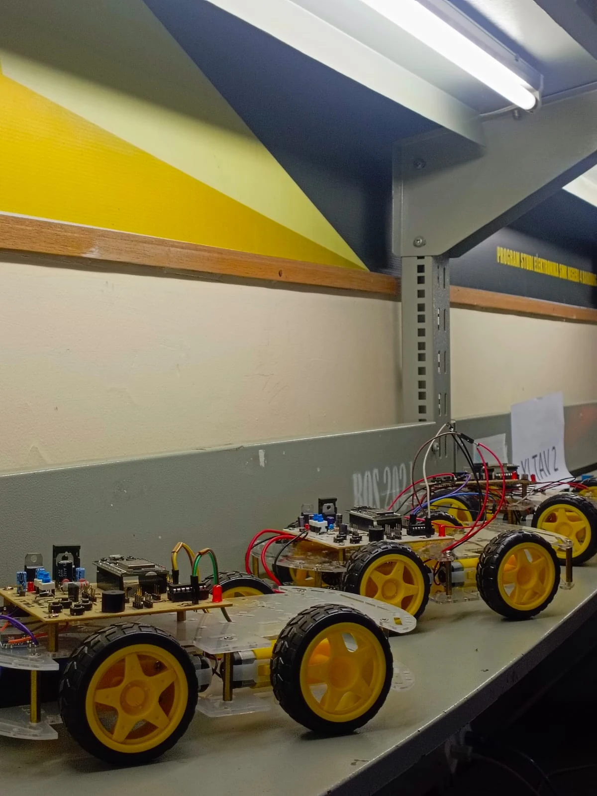 Robot 4WD wireless dengan mikrokontroler dan empat roda kuning di laboratorium robotika